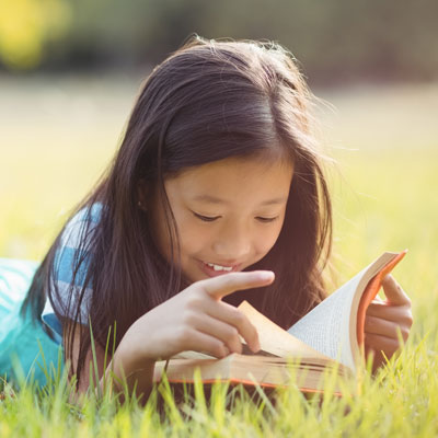 girl lying in grass reading book on sunny day