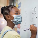 schoolgirl solving addition problem on white board during Covid-19 pandemic